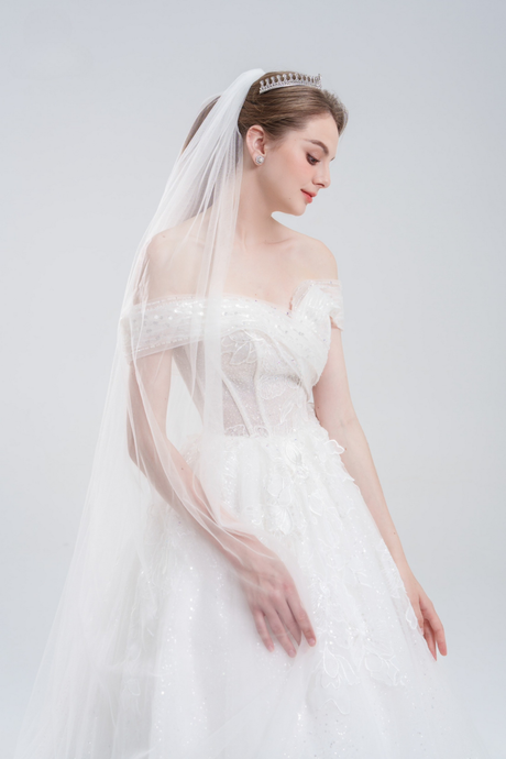 Off-the-shoulder ball gown wedding dress with sparkling tulle, intricate beadwork, and a voluminous skirt for a glamorous fairytale look.