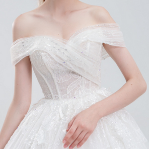 Off-the-shoulder ball gown wedding dress with sparkling tulle, intricate beadwork, and a voluminous skirt for a glamorous fairytale look.
