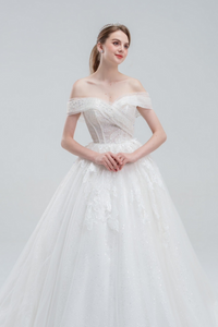 Off-the-shoulder ball gown wedding dress with sparkling tulle, intricate beadwork, and a voluminous skirt for a glamorous fairytale look.